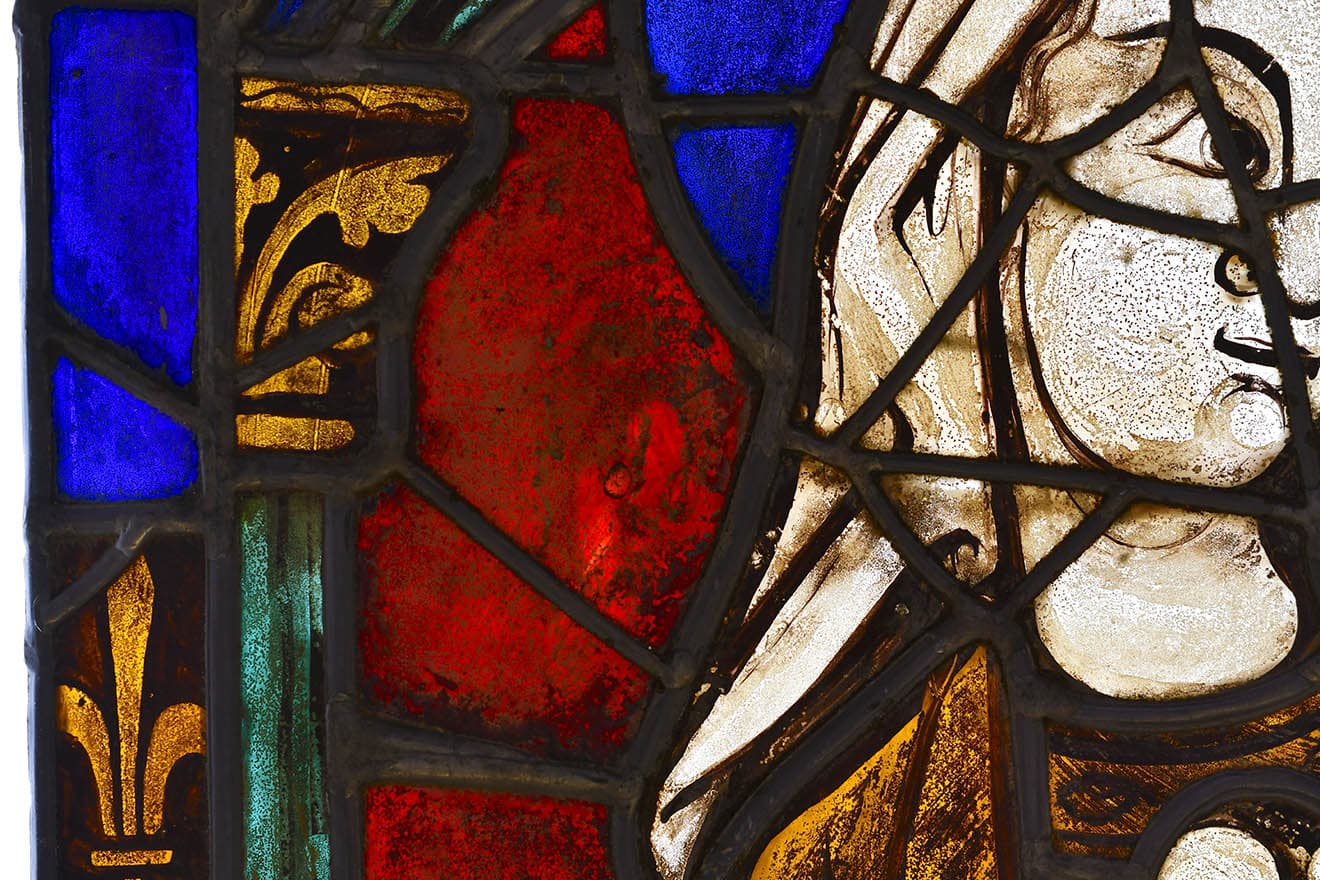 Portion of a stained glass window, blue, red and yellow glass, a women's face, hair, shoulder and gold gown.